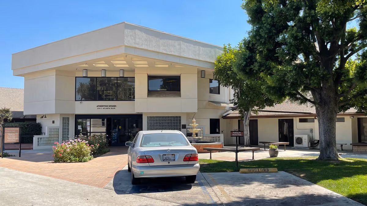 The front entrance of Atherton Baptist Homes with a parked car, fountain, and trees on a sunny day.