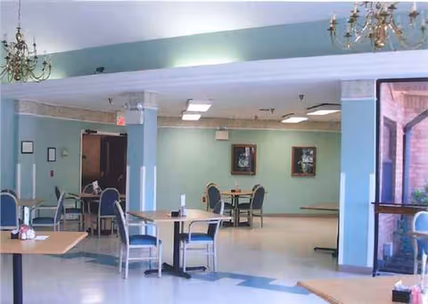 Empty senior living dining room with tables, chairs, and teal walls.