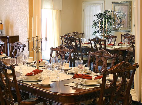 Formally set dining room with wooden tables and chairs, place settings, glassware, and candelabras.