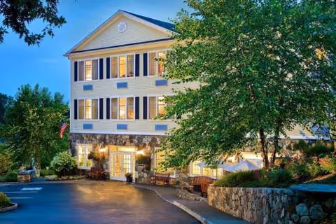 Three-story senior living building with lit entrance, trees, and a parking lot.