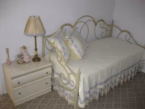 Cream metal bed with ornate headboard and matching nightstand in a cozy bedroom.
