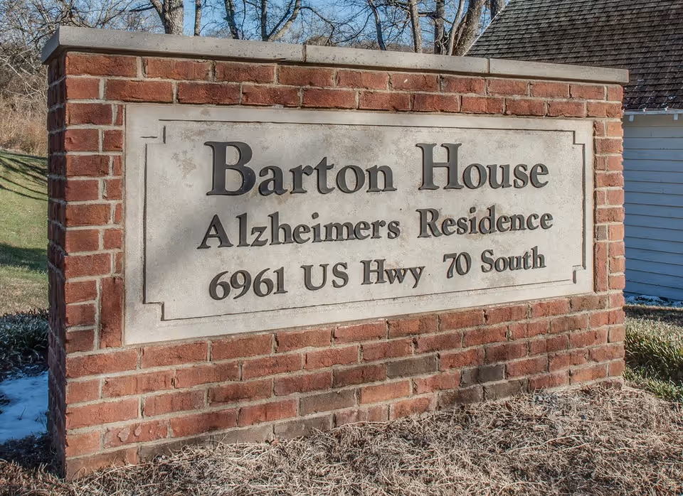 Brick entrance sign reading 'Barton House Alzheimer's Residence 6961 US Hwy 70 South' on a lawn.