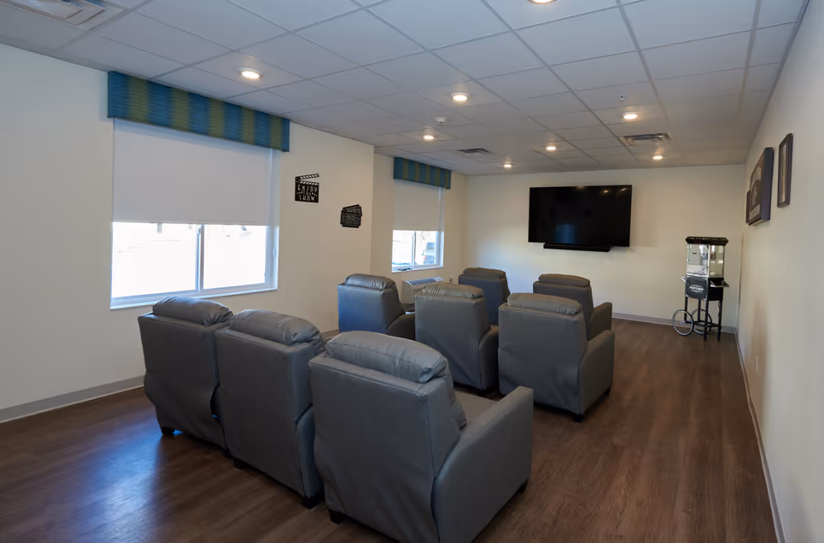 Small screening room with two rows of gray recliners facing a wall-mounted TV and a popcorn machine.