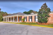 Single-story brick building with a covered portico entrance, driveway and landscaped shrubs and trees.