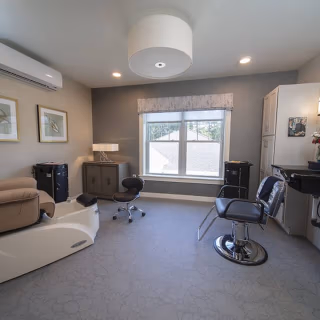 Bright salon-style room with a pedicure chair, styling chairs, cabinetry and a large window.