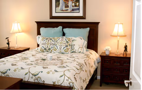 A neatly made bed with a patterned duvet, decorative pillows, wooden headboard and matching nightstands with lamps in a bedroom.