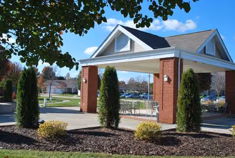 Brick-adorned senior living entrance with arched roof, columns, and outdoor seating under awning.