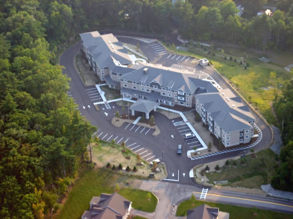 Aerial view of the Ledgewood Bay Assisted Living complex surrounded by trees with parking lots and driveways.
