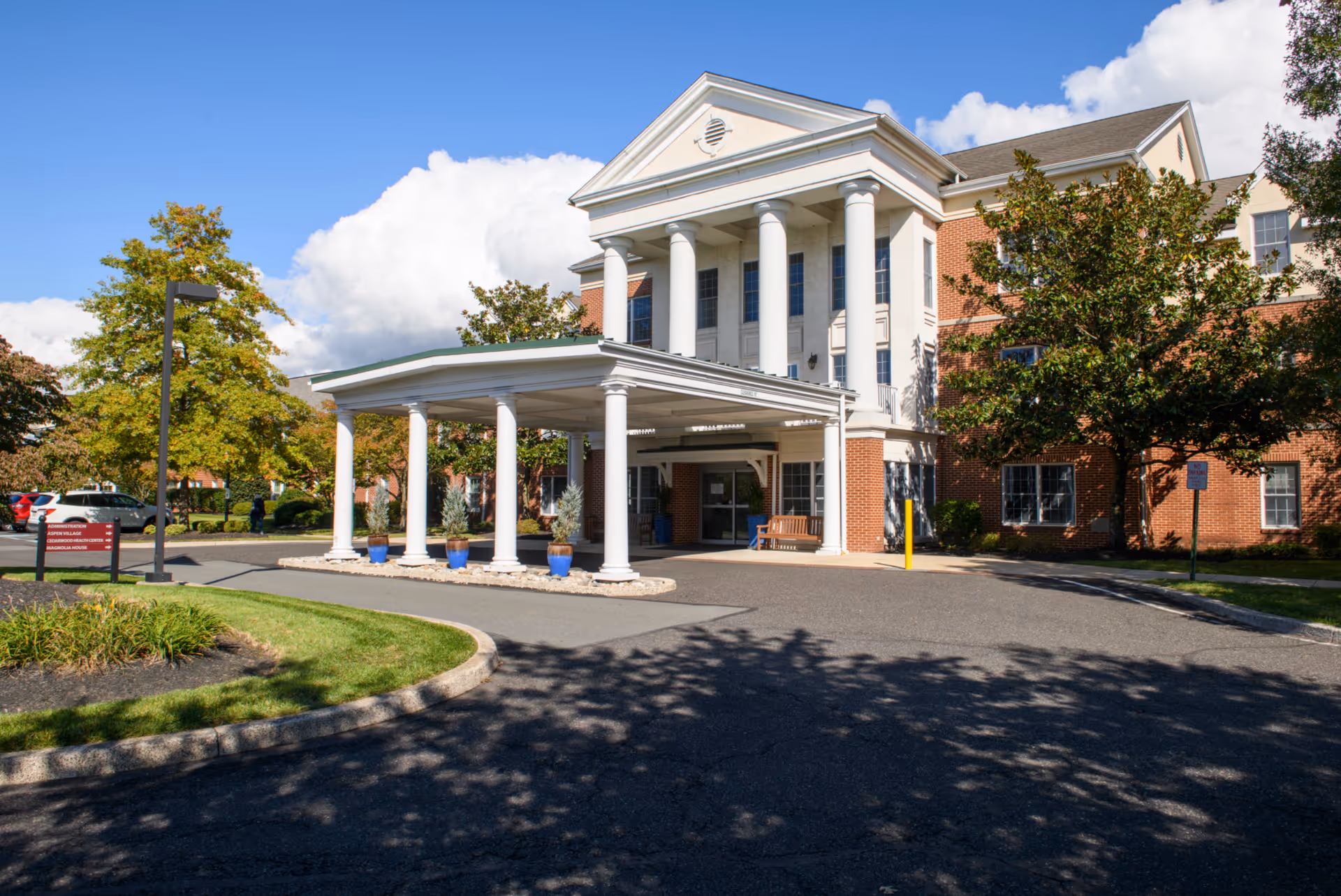 Front entrance of a red-brick senior living building with white columns and a covered porte-cochere.
