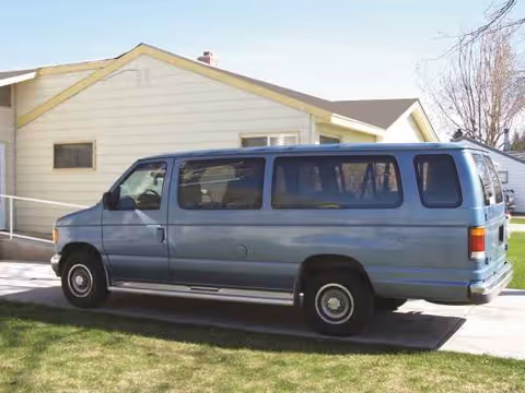 Blue passenger van parked on a driveway beside a beige single-story building.