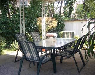 Outdoor patio with striped cushioned chairs around a glass-top table under a canopy.