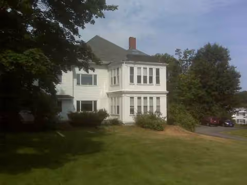 White two-story senior living facility with bay windows and a grassy lawn.