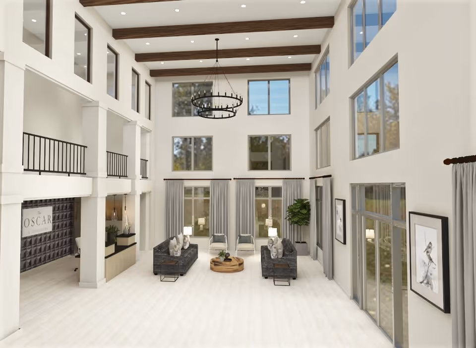 Spacious and modern living room area with high ceilings, large windows, and exposed wooden beams. The room features two dark gray sofas facing each other with a round wooden coffee table in the center, two armchairs near the windows, floor lamps, and framed artwork on the walls. A chandelier hangs from the ceiling, and there is a reception desk area with a sign that reads 'The Oscar' on the left side.