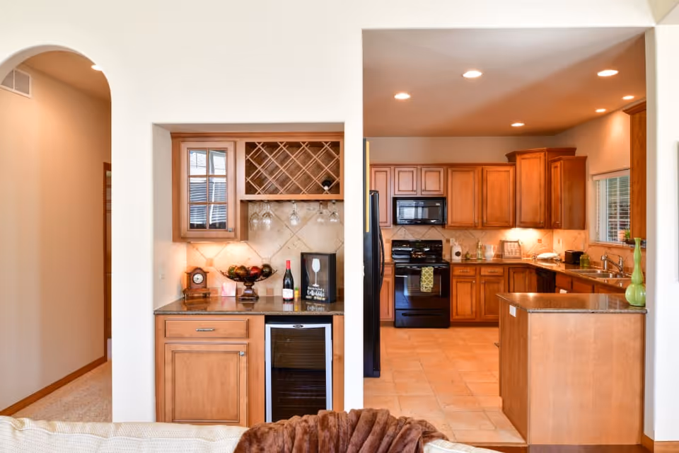 Open-concept kitchen and wet bar with wooden cabinets, a central island, and a wine rack visible from the living area.