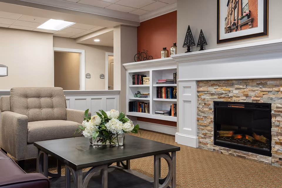 A comfortable lounge area with an armchair, coffee table with a floral arrangement, built-in bookshelves and a stone-front fireplace.