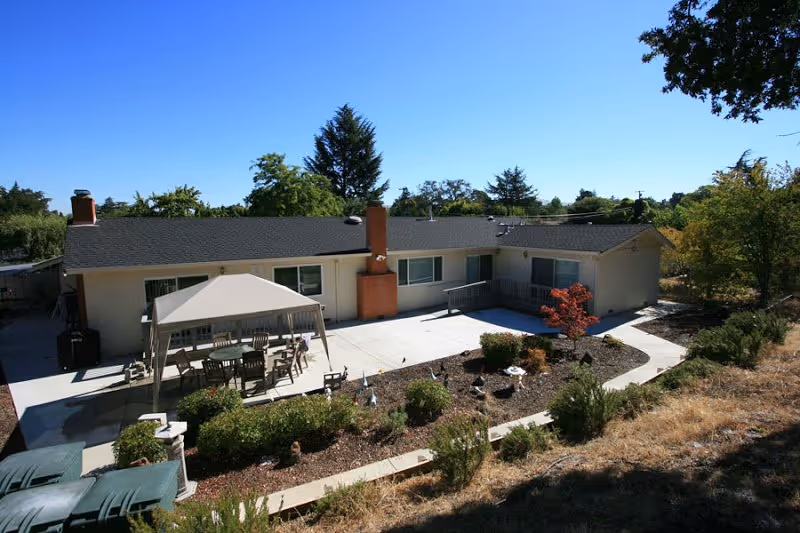 Exterior of a senior living facility with a shaded patio and landscaped courtyard.