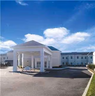 White building with a portico entrance and blue sky above at Belair Care Center.