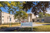 Exterior view of Highland Rehabilitation & Nursing Center building with a sign in front on a grassy area, trees around, and a clear blue sky.