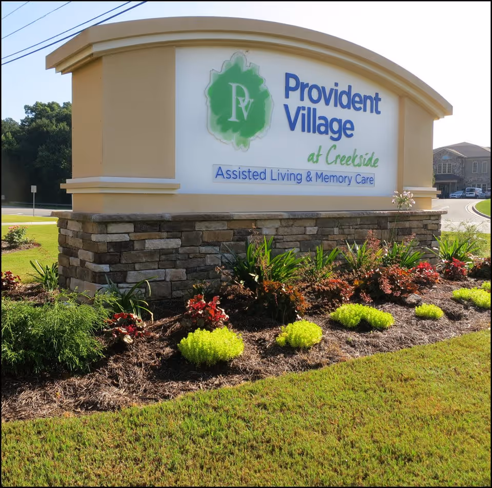 Entrance sign reading 'Provident Village at Creekside Assisted Living & Memory Care' mounted on a stone base with landscaped plants in front.