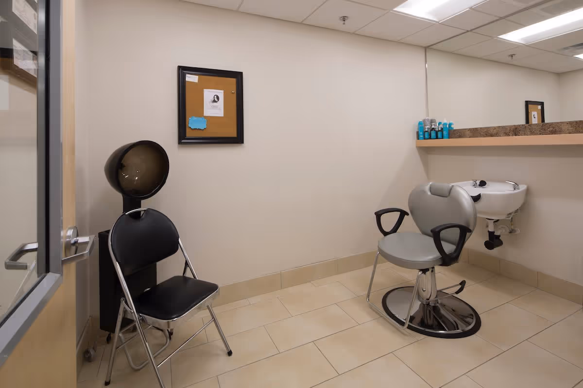 Small hair salon room with a styling chair and sink, a hooded dryer, a folding chair, and a counter with products.