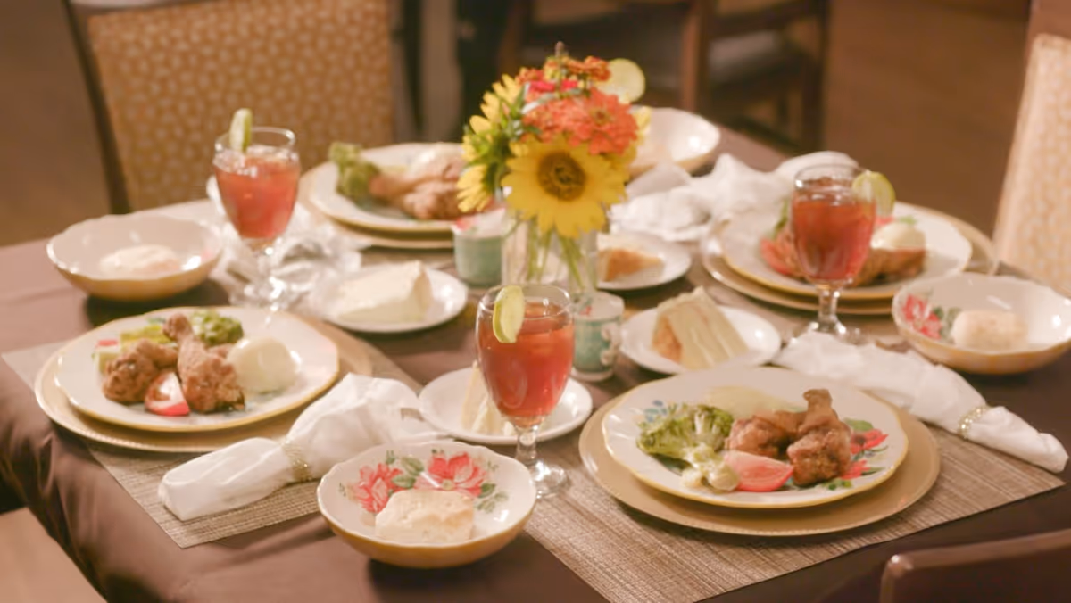 A dining table set with plated meals, iced tea glasses with lime, napkins, and a small floral centerpiece.