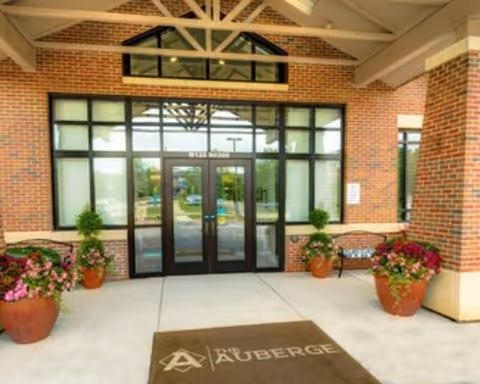 Covered brick entrance with glass double doors, potted plants, and a doormat reading "The Auberge".