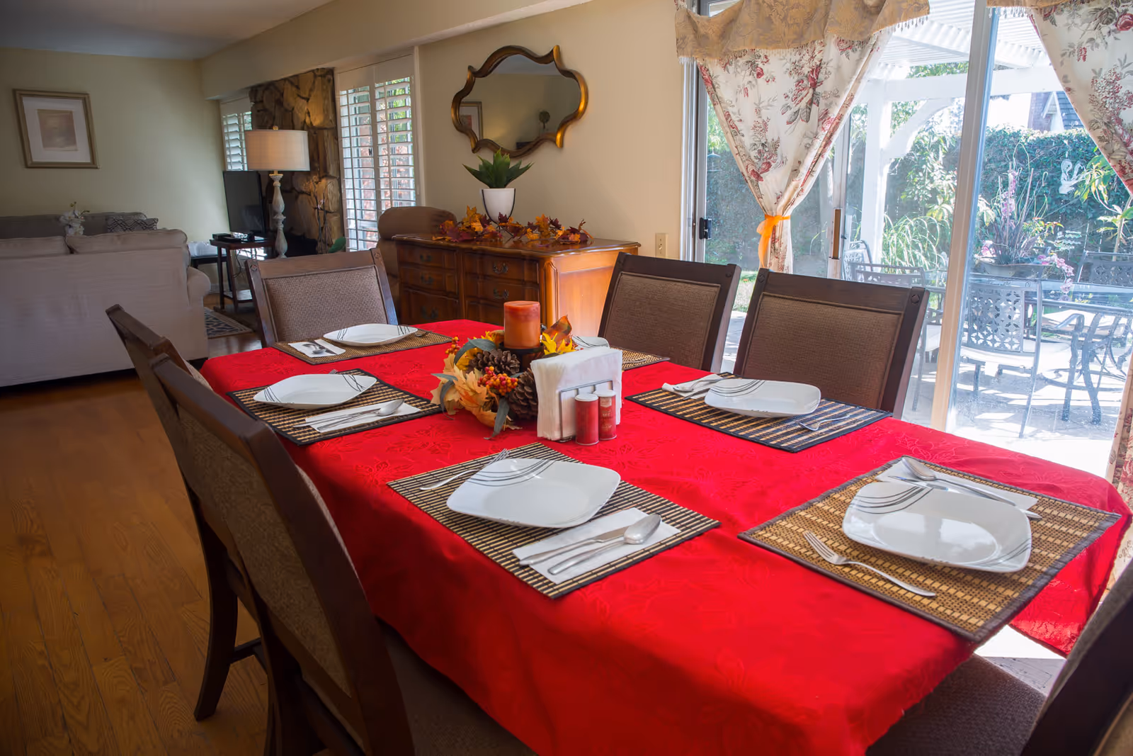 Dining room with a red-tablecloth table set for six, chairs, sideboard and sliding glass doors looking out to a patio.