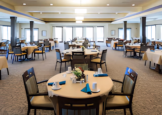 Large communal dining room with multiple round tables set with place settings and chairs.