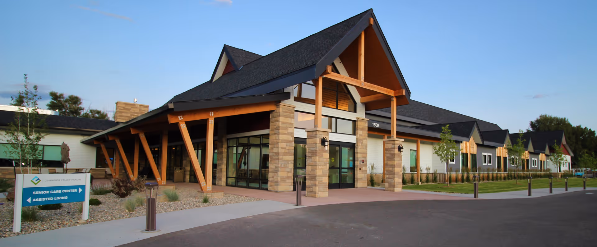 Front exterior of Gunnison Valley Health Senior Care Center showing a covered entrance with timber beams and landscaped grounds.