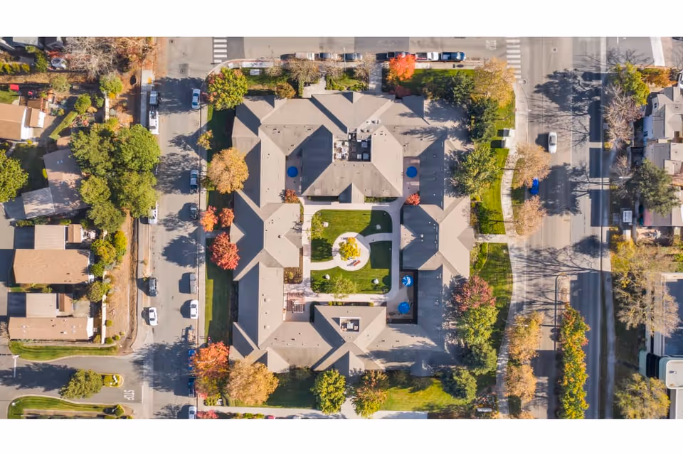 Aerial view of a courtyard-centered memory care complex with surrounding streets, trees, and parked cars.