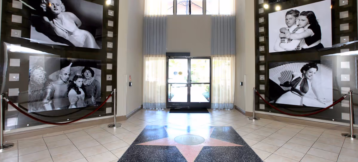 Bright, high-ceiling lobby with a star-patterned floor, large black-and-white photo panels on both walls, velvet ropes and glass double doors at the entrance.