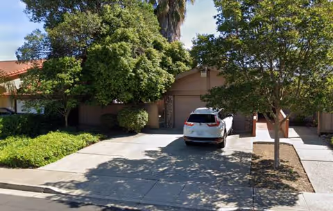 Exterior view of Trinity Manor with a parked car, driveway, and trees.