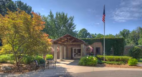 Entrance to a senior living facility with a covered entry, flagpole, and landscaped outdoor seating.