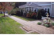 Brick walkway bordered by grass and landscaping leading to a covered entrance and fountain in front of a single-story building.