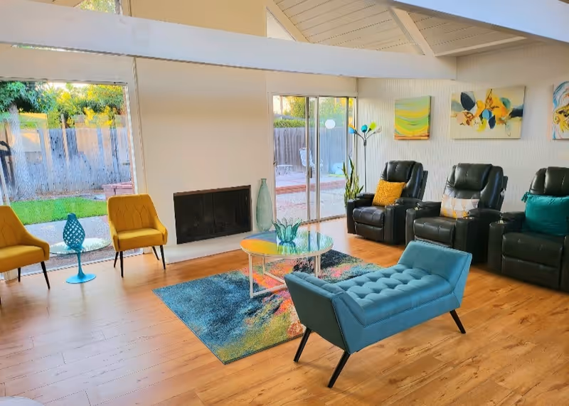 Bright senior living lounge with colorful chairs, leather recliners, fireplace, and glass sliding doors.