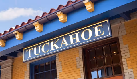 Exterior view of a brick building facade with a blue sign reading "TUCKAHOE" beneath a tiled roof.