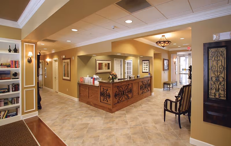 Reception desk and lobby area with seating, bookshelves, and warm lighting in a senior living facility.