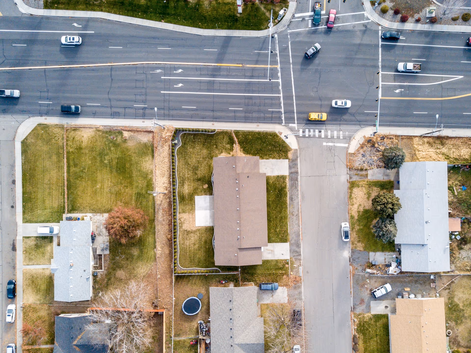 Aerial view of a residential neighborhood showing several houses with yards, streets, and cars driving on a main road and side streets.