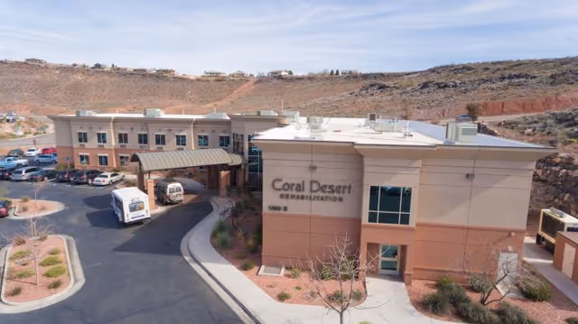 Front exterior of the Coral Desert Rehabilitation and Care building showing its covered entrance, parked vehicles, and surrounding desert hills.