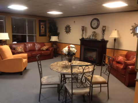 Cozy lounge with red leather sofas, a round table, and a decorative fireplace.