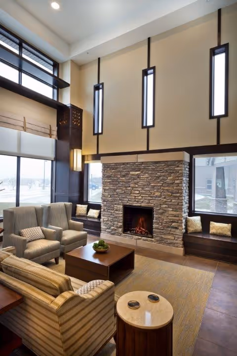 Bright lounge with high ceilings centered on a stone fireplace, seating area with armchairs, sofa, coffee table and large windows.