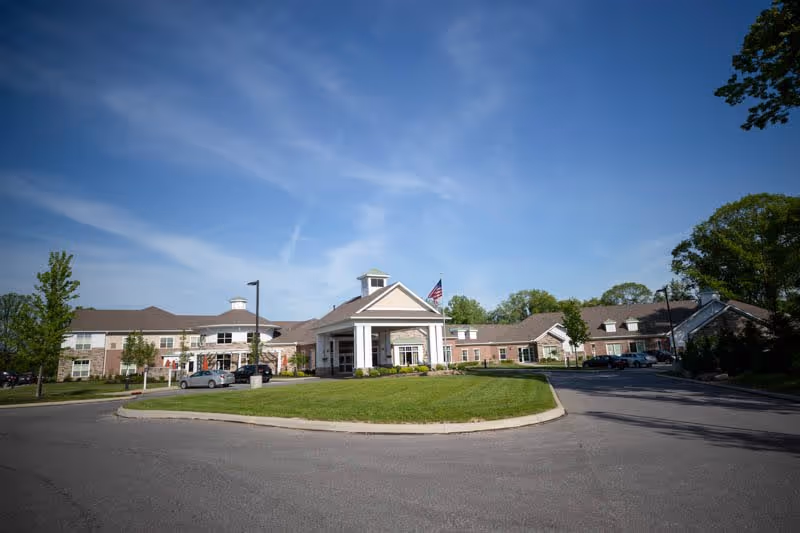 Front entrance of the Vista Springs Ravinia Estate building with a circular drive, manicured lawn, and an American flag under a blue sky.