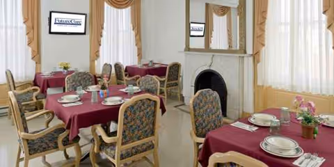 Senior living dining room with burgundy tablecloths, upholstered chairs, place settings, and a fireplace.