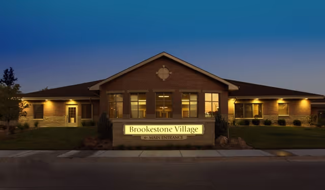 Front exterior of Brookestone Village building at dusk with an illuminated main entrance sign.