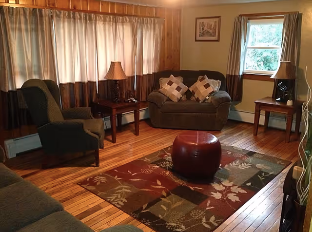 Cozy living room with wood floors, a patterned area rug, armchairs and a loveseat flanked by side tables and lamps.