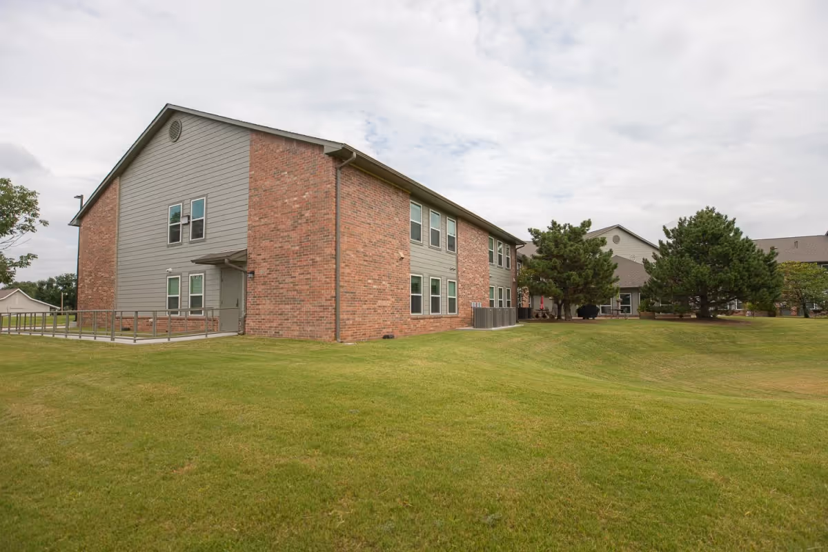 Exterior view of a brick and gray siding senior living building with a wide grassy lawn and trees.