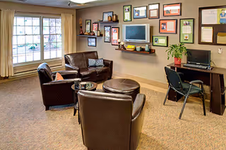 Cozy lounge area with leather chairs, a wall gallery, and a desk in a facility.