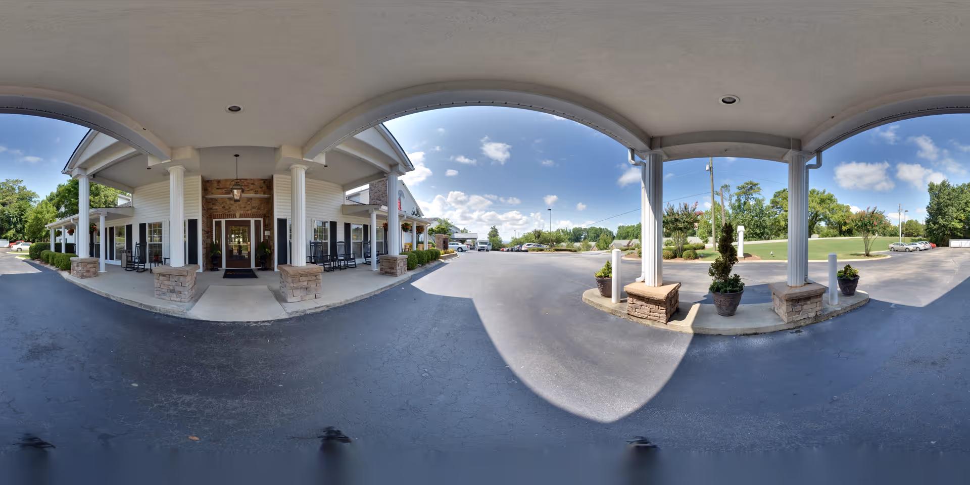 Covered front entrance with white columns, seating and potted plants under a porte-cochere opening onto a driveway.