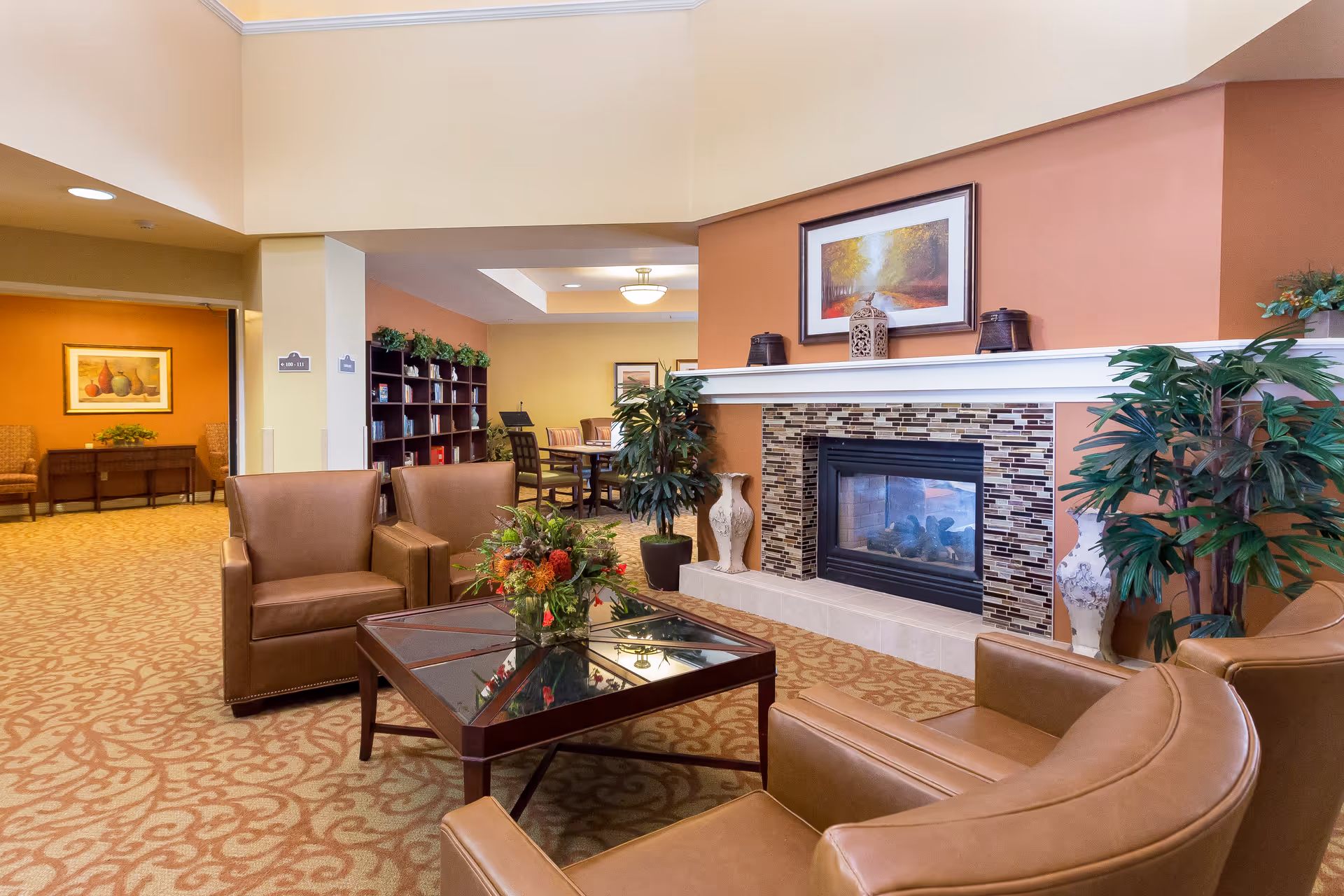 Cozy senior living lounge with leather chairs around a glass coffee table and a tiled fireplace.