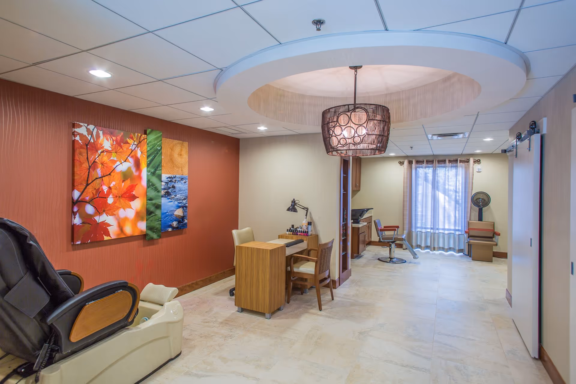 Bright interior salon/lounge area with a manicure table, salon chairs, a massage chair and colorful wall art.